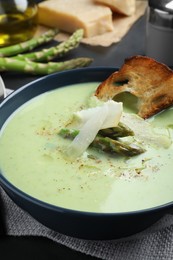 Photo of Bowl of delicious asparagus soup served on dark table, closeup