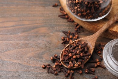 Photo of Glass jar and spoon with aromatic cloves on wooden table. Space for text