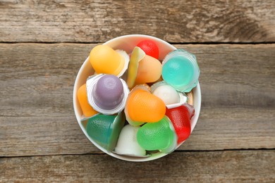Photo of Bowl with tasty bright jelly cups on wooden table, top view