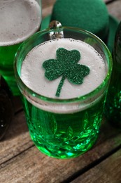 Photo of St. Patrick's day party. Green beer with decorative clover leaf and leprechaun hat on wooden table, closeup
