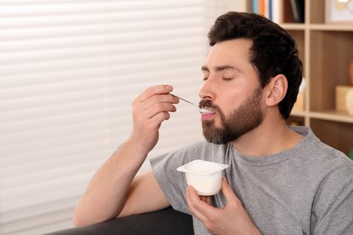 Photo of Handsome man eating delicious yogurt at home. Space for text