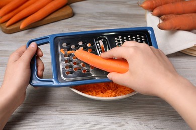 Photo of Woman grating fresh carrot at wooden table, closeup