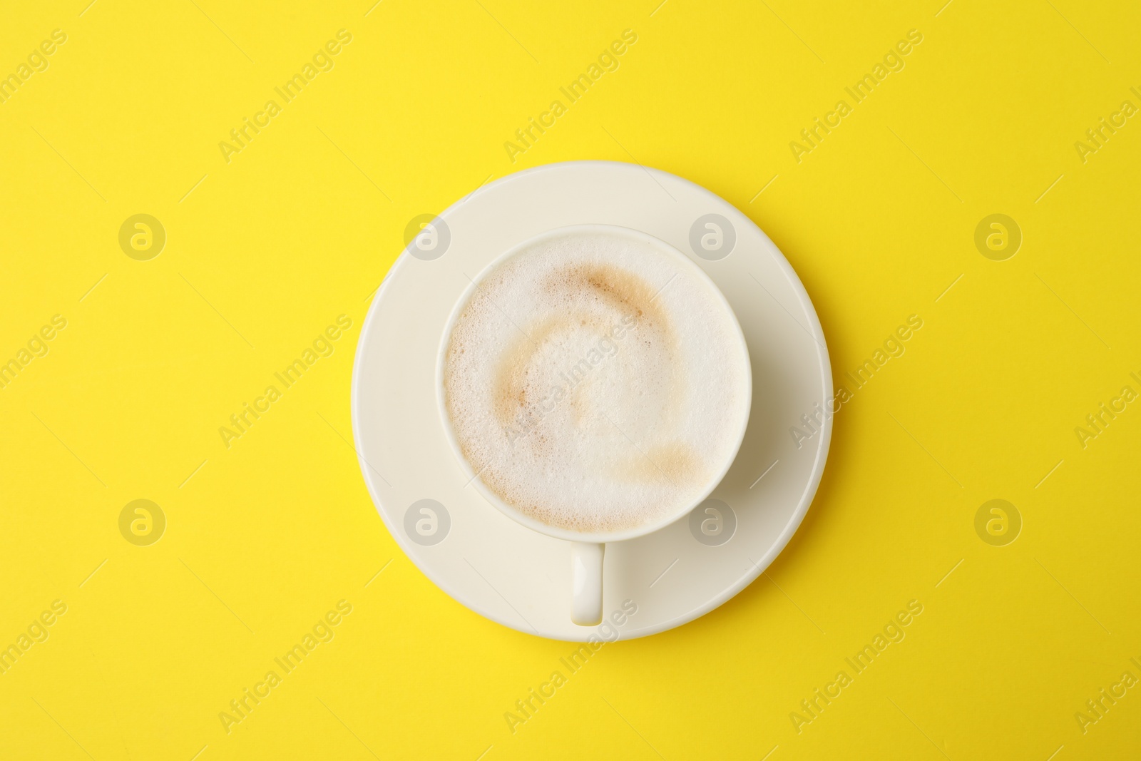 Photo of Tasty cappuccino in coffee cup on yellow background, top view