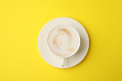 Photo of Tasty cappuccino in coffee cup on yellow background, top view