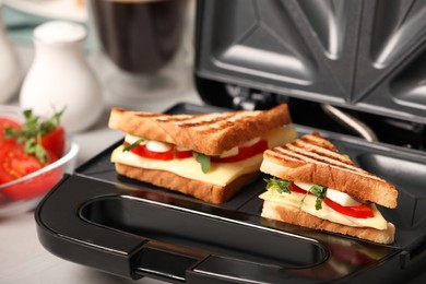 Photo of Modern grill maker with sandwiches on table, closeup view