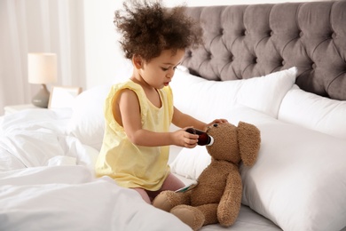 Photo of Cute African American child imagining herself as doctor while playing with toy bunny at home