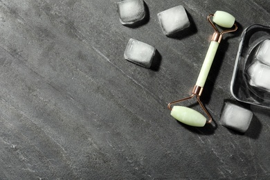 Photo of Natural jade face roller and ice cubes on grey background, flat lay. Space for text