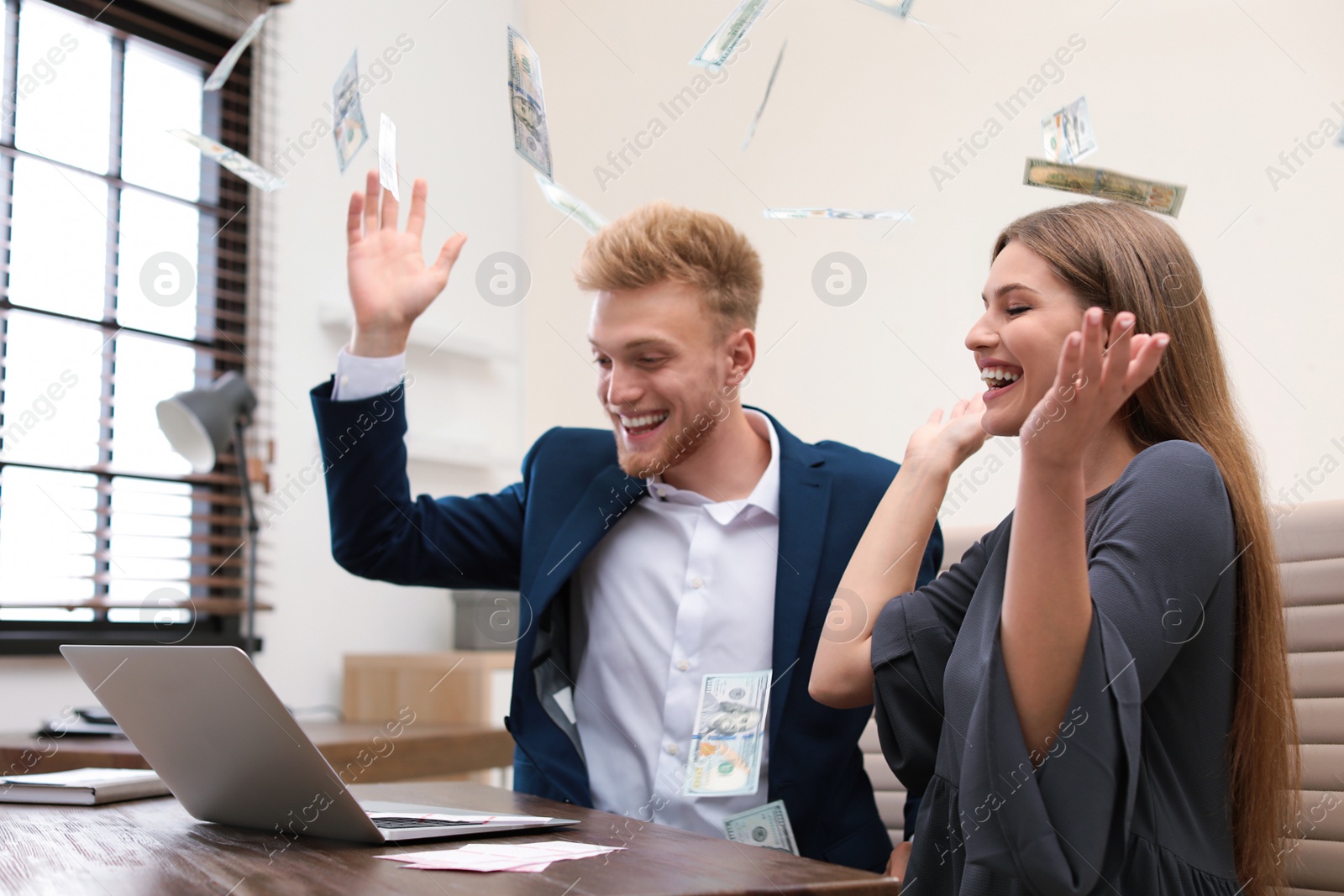 Photo of Happy young people playing online lottery using laptop under money rain in office