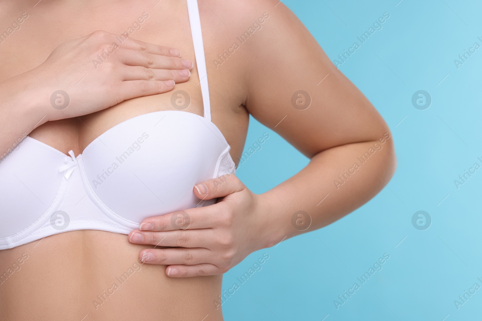 Photo of Mammology. Woman in bra doing breast self-examination on light blue background, closeup