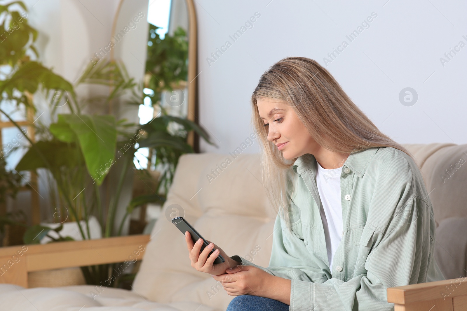 Photo of Woman using smartphone on sofa at home. Space for text