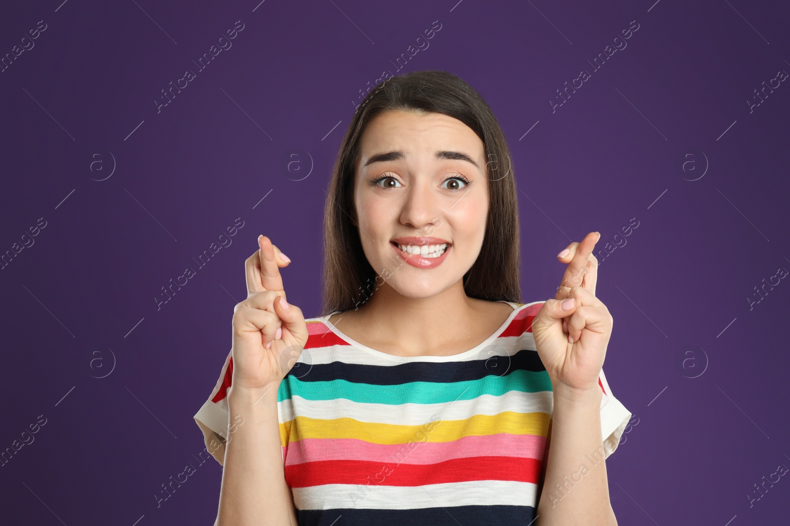 Photo of Woman with crossed fingers on purple background. Superstition concept