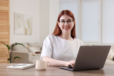 Photo of Happy woman using laptop at wooden table in room