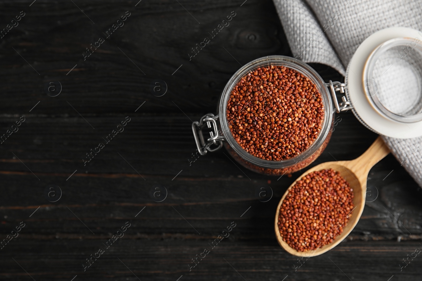 Photo of Spoon and jar with red quinoa on black wooden background, top view. Space for text