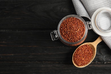 Spoon and jar with red quinoa on black wooden background, top view. Space for text