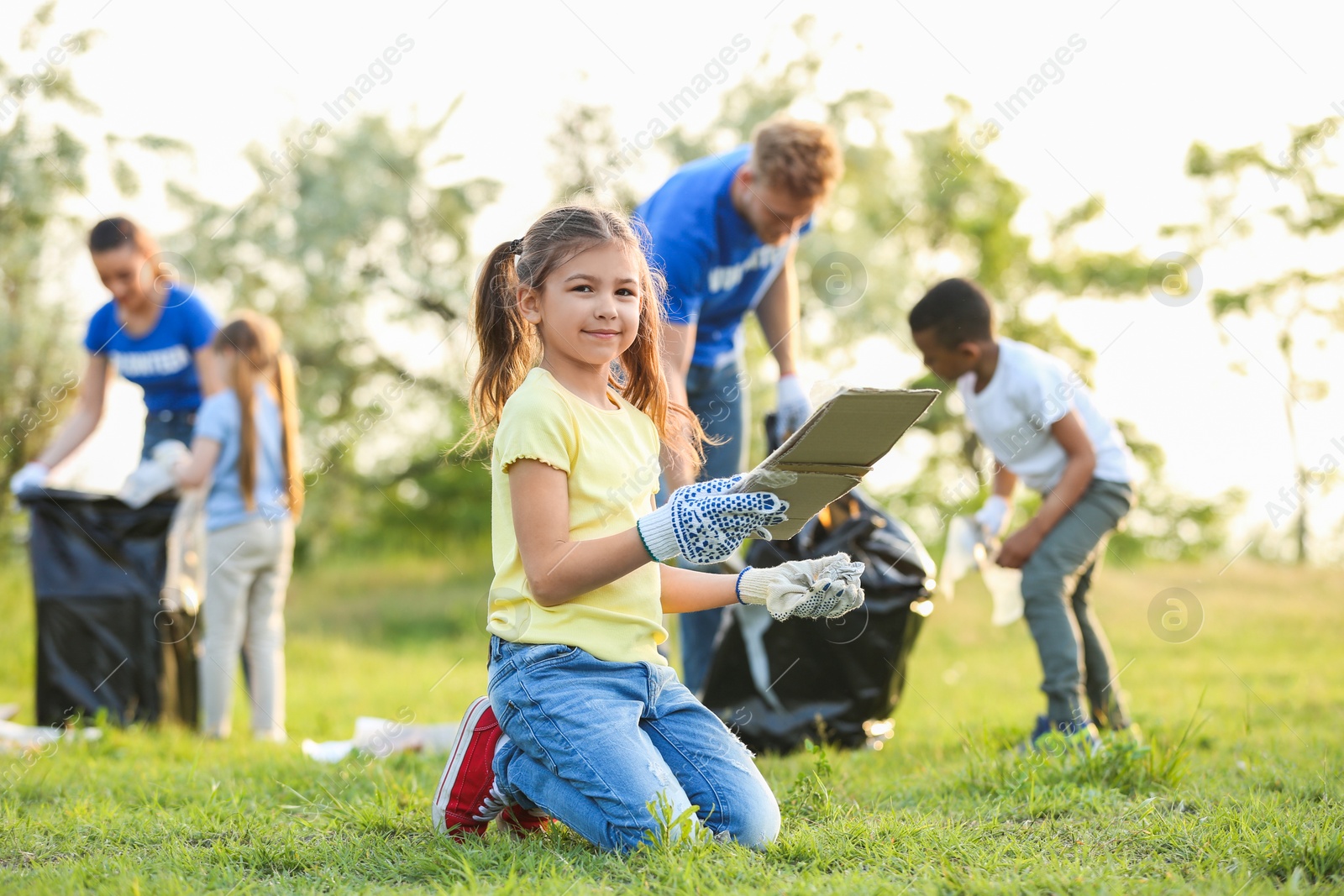 Photo of Little girl collecting trash in park. Volunteer project