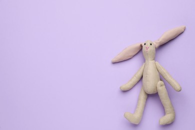 Toy bunny on lilac background, top view. Space for text