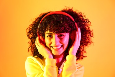 Beautiful young woman listening to music with headphones on color background in neon lights
