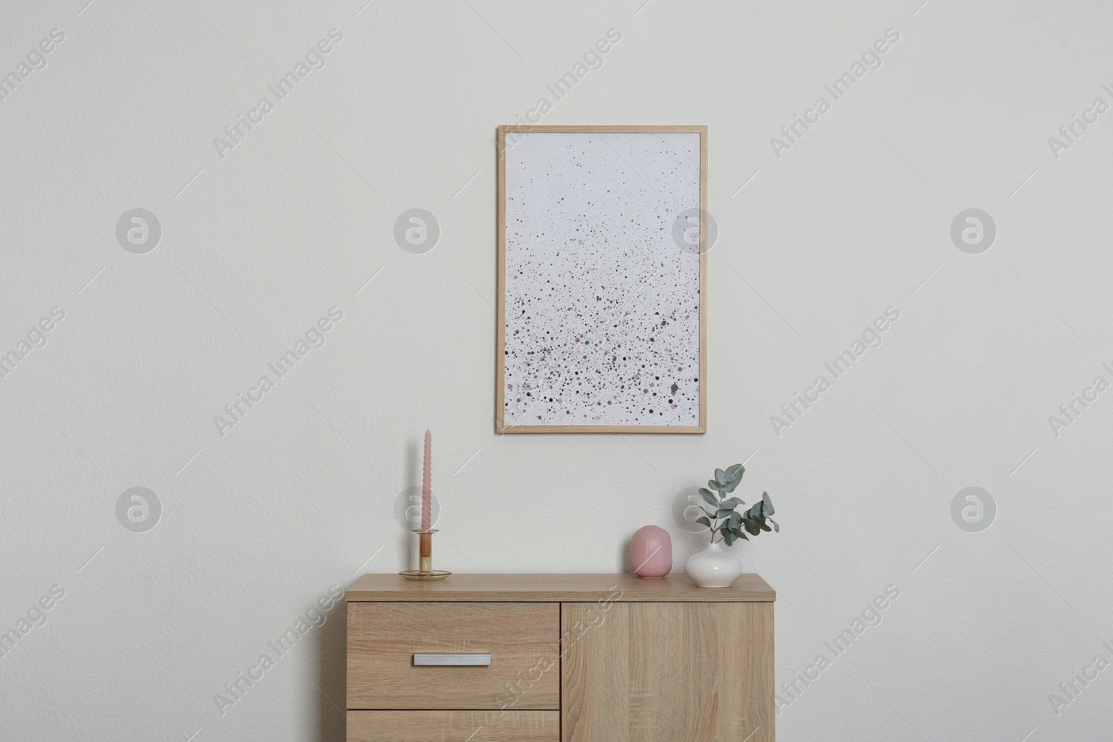 Photo of Chest of drawers, decorative elements and frame in room with light wall. Interior design