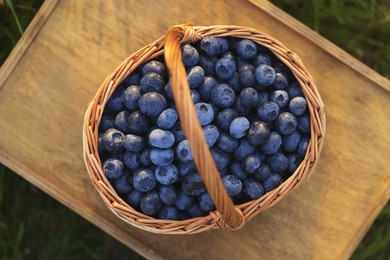 Photo of Wicker basket of tasty ripe blueberries on wooden surface outdoors, top view. Seasonal berries