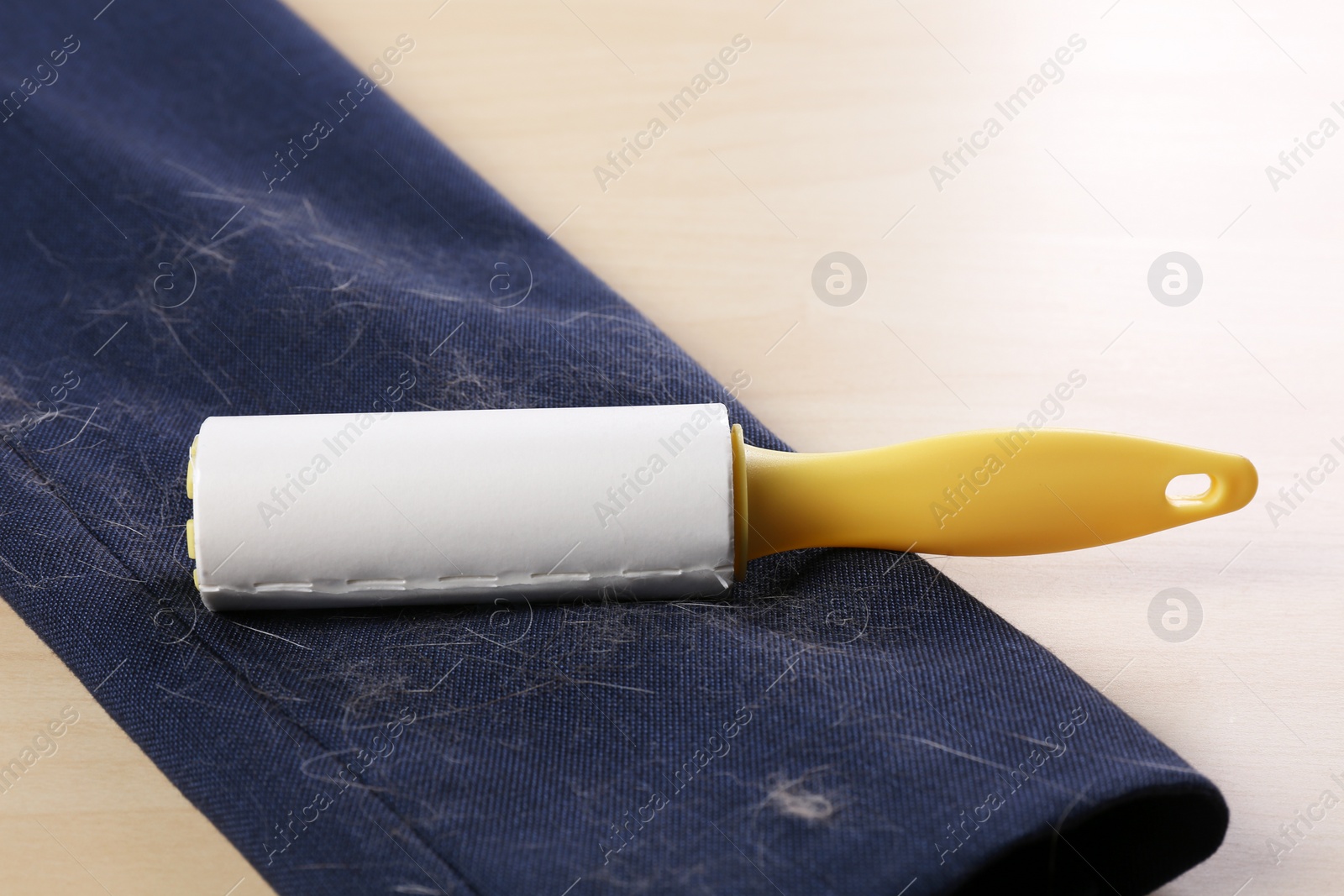 Photo of Lint roller and sleeve of jacket covered with hair on wooden table