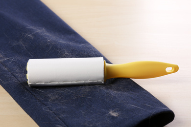 Photo of Lint roller and sleeve of jacket covered with hair on wooden table