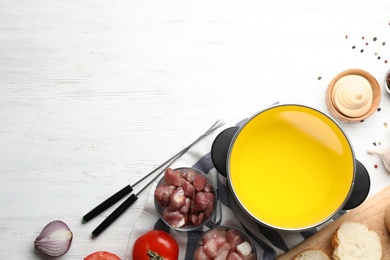 Flat lay composition with oil pot, meat fondue ingredients and space for text on wooden background