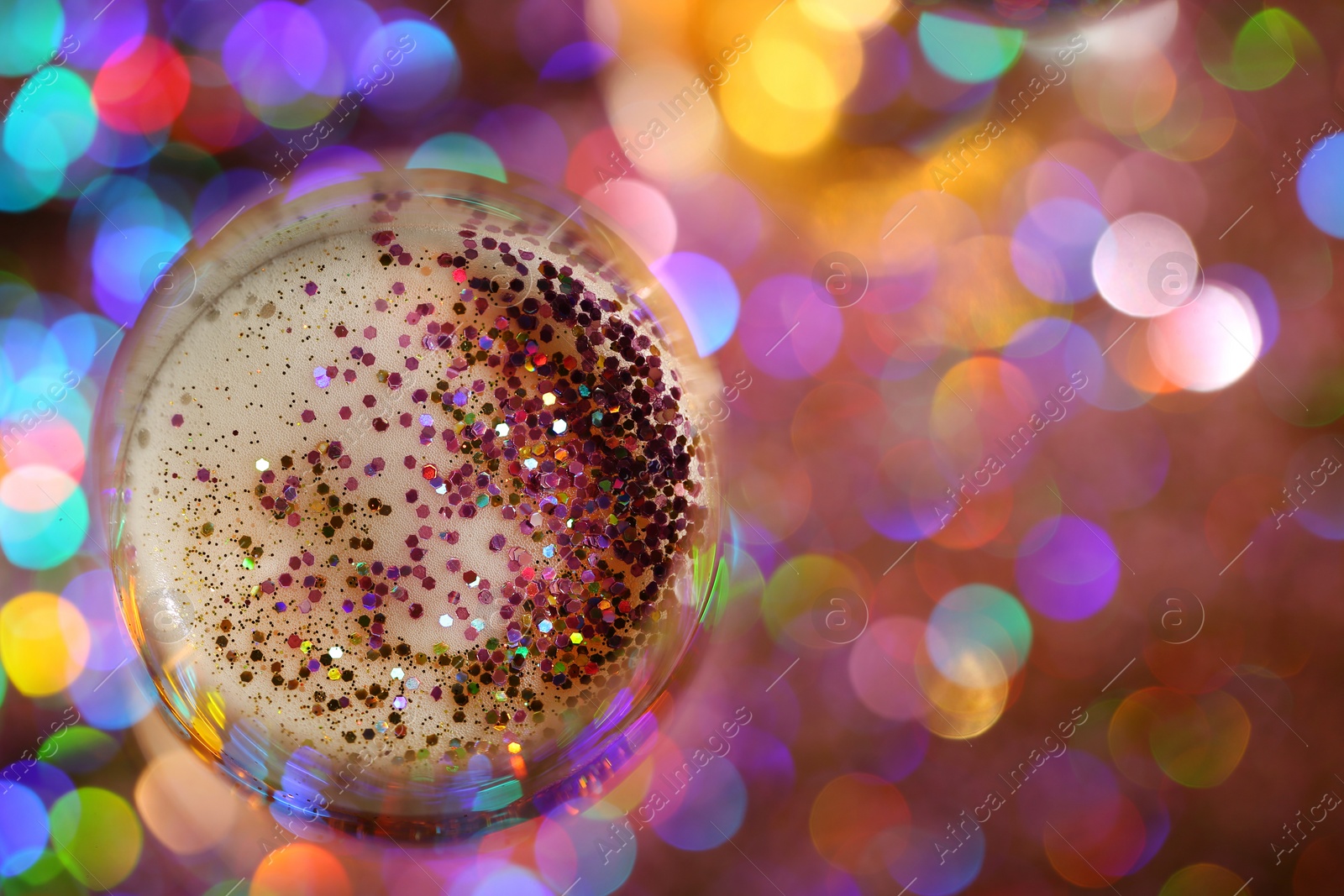 Photo of Glass of champagne with rose gold glitter on blurred background, top view. Space for text