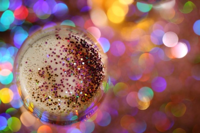 Glass of champagne with rose gold glitter on blurred background, top view. Space for text