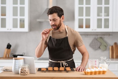 Man with freshly baked cookies watching online cooking course via tablet in kitchen