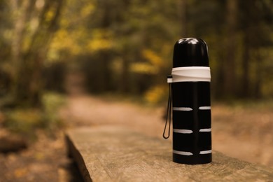 Black thermos on wooden bench outdoors, space for text