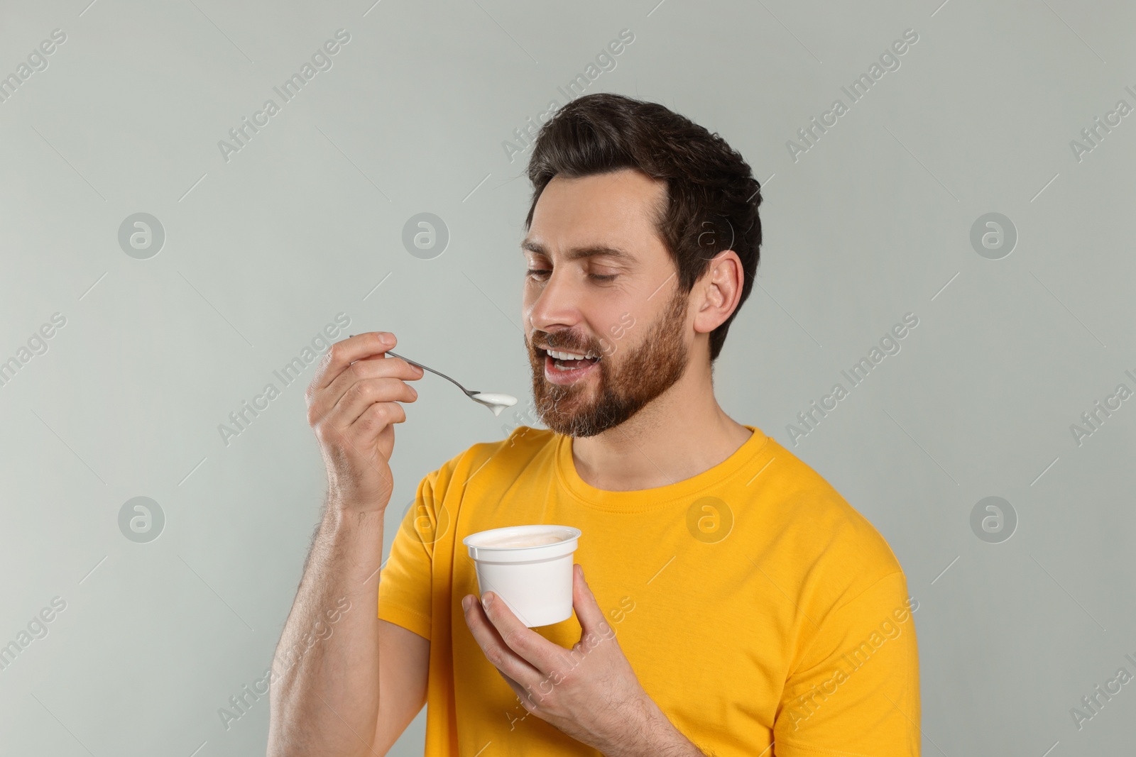 Photo of Handsome man eating delicious yogurt on light grey background