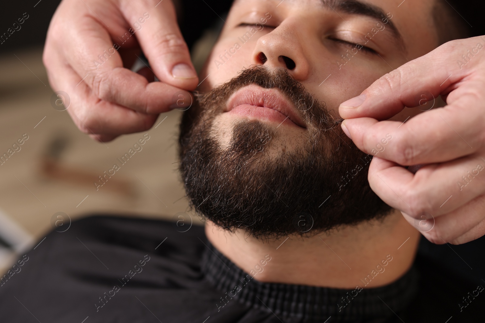 Photo of Professional barber working with client's mustache in barbershop, closeup