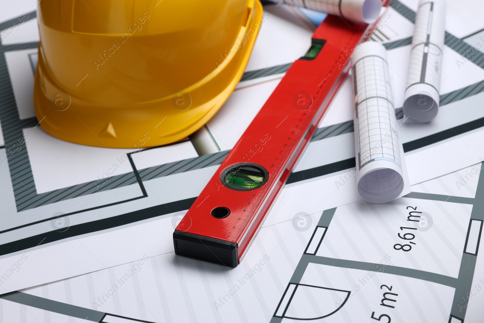 Photo of Construction drawings, safety hat and bubble level on house plan, closeup