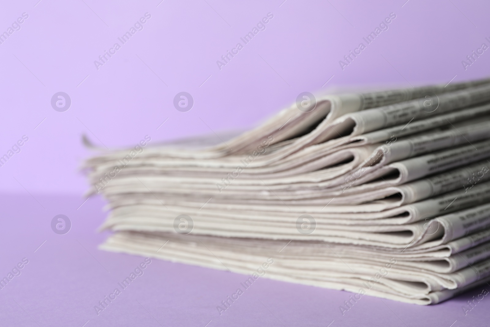 Photo of Stack of newspapers on light violet background, closeup. Journalist's work