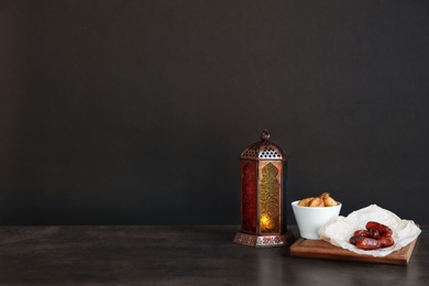 Photo of Muslim lantern Fanous and dried fruits on table against dark background. Space for text