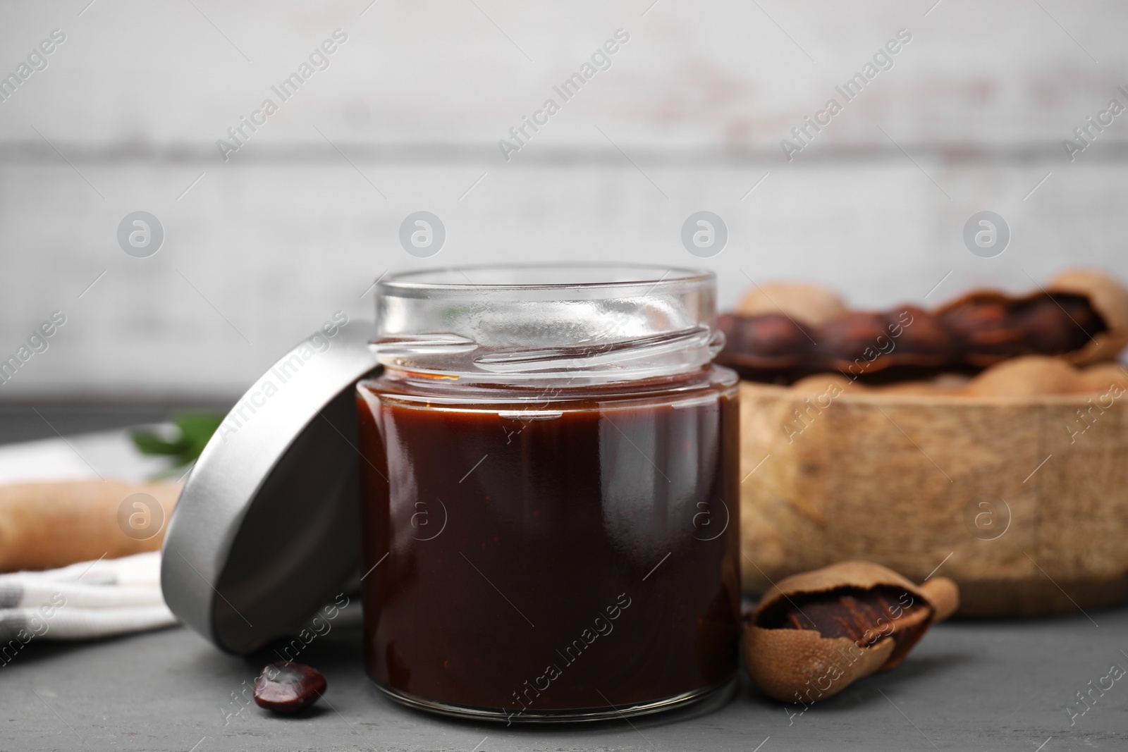 Jar of tasty tamarind sauce and fresh pods on grey wooden table Photo of Jar of tasty tamarind sauce and fresh pods on grey wooden table