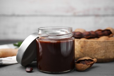 Photo of Jar of tasty tamarind sauce and fresh pods on grey wooden table
