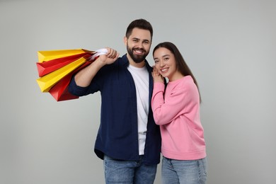 Happy couple with shopping bags on grey background