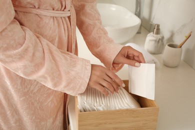 Photo of Woman taking disposable menstrual pad from wooden box in bathroom, closeup
