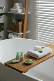 Photo of Wooden tray with spa products on bath tub in bathroom