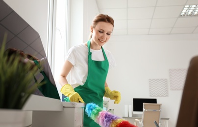 Young woman in apron and gloves cleaning office
