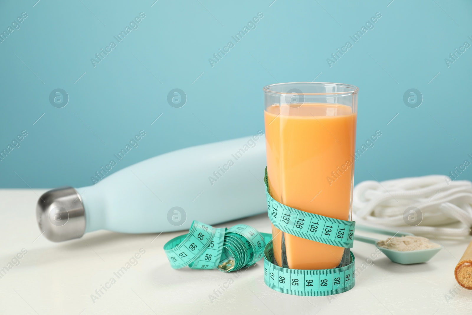 Photo of Tasty shake, bottle, measuring tape and powder on white table against light blue background. Weight loss