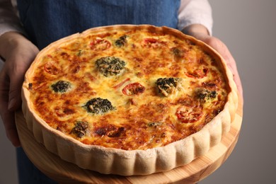 Woman holding delicious homemade vegetable quiche on light gray background, closeup