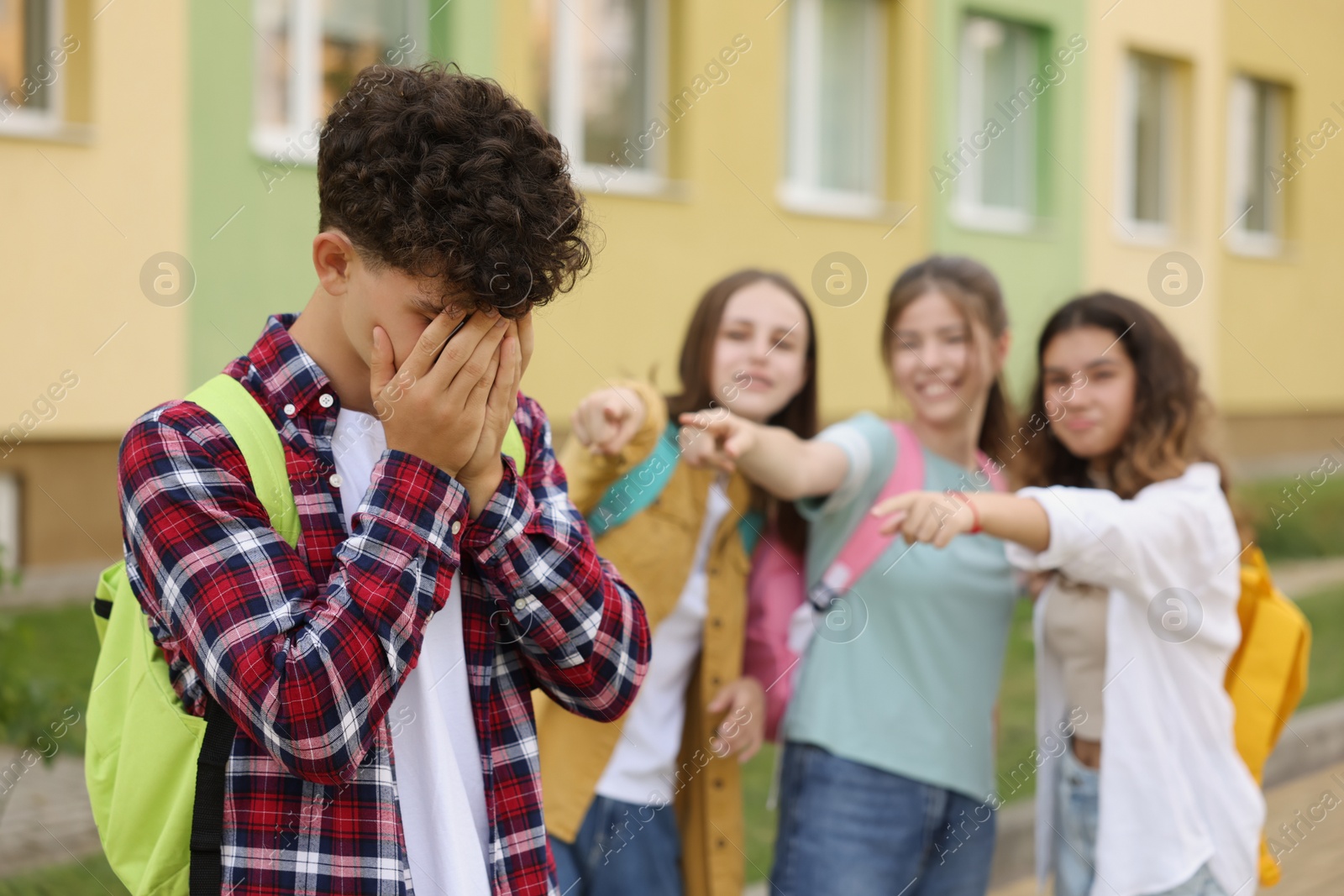 Photo of Teen problems. Group of students pointing at upset boy outdoors, selective focus