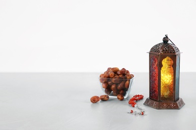 Photo of Muslim lamp, dates and prayer beads on table against white background. Space for text