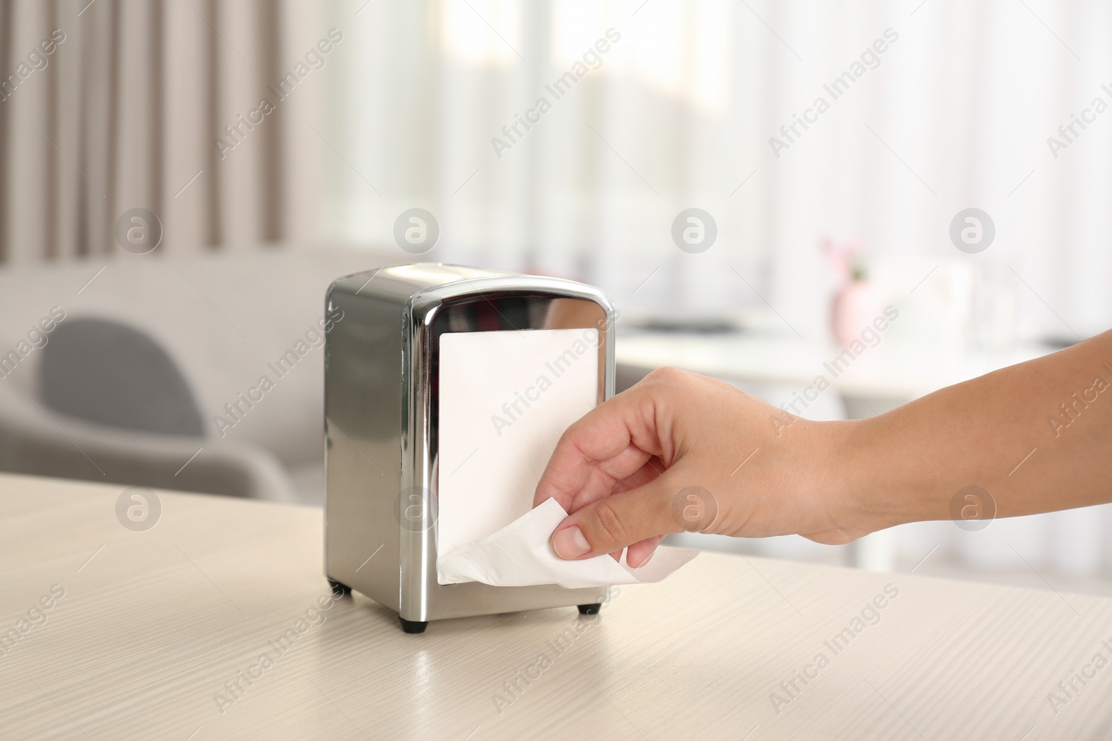 Photo of Woman taking paper tissue from napkin holder on table