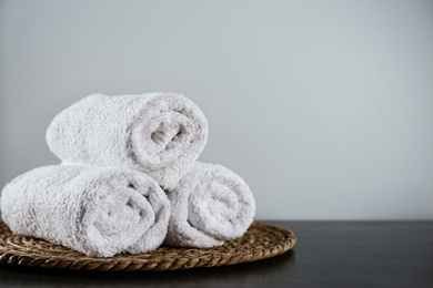 Photo of Clean rolled bath towels and wicker mat on dark grey table. Space for text