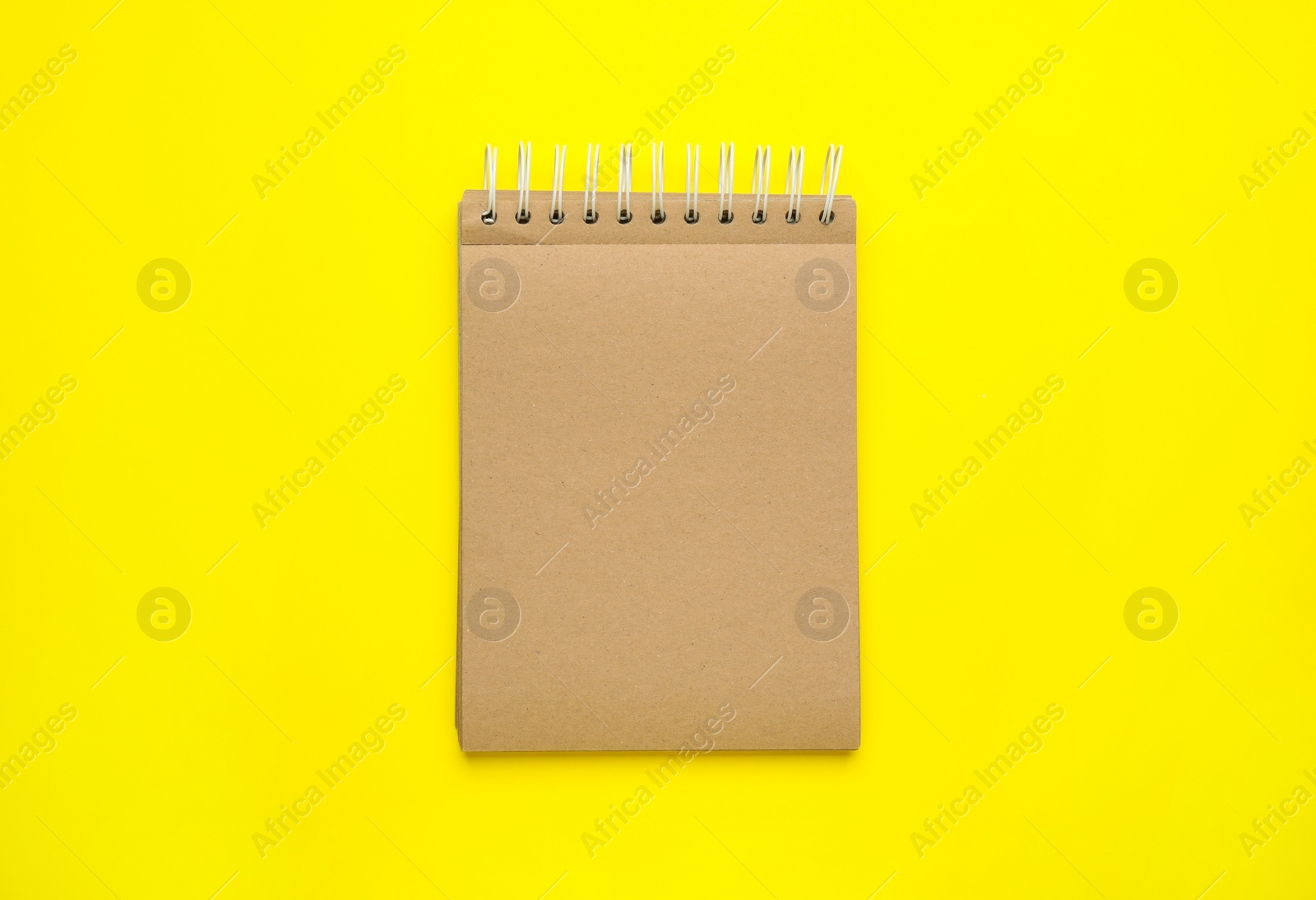 Photo of Notebook with brown paper pages on yellow background, top view