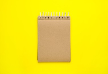 Photo of Notebook with brown paper pages on yellow background, top view