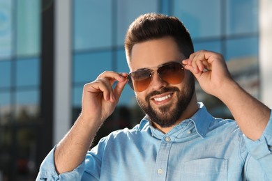 Handsome smiling man in sunglasses outdoors on sunny day, space for text